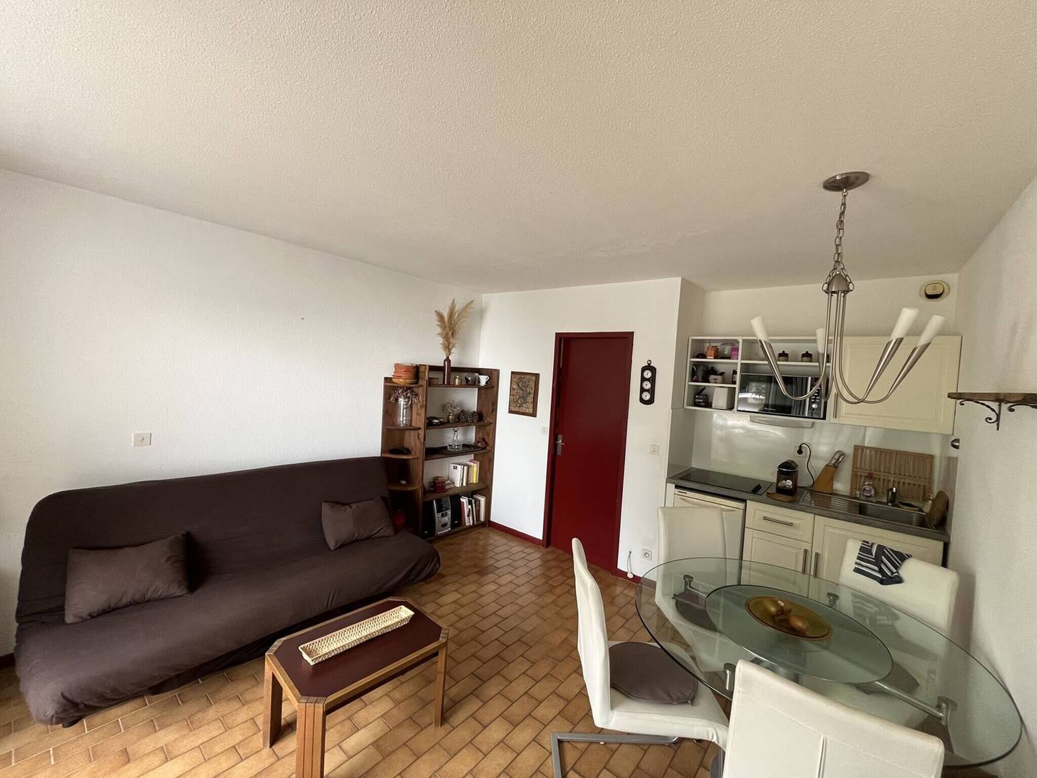 Un salon avec un canapé marron, une table basse en verre et un coin repas comprenant une table et des chaises en verre.