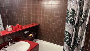 Un bagno con un lavandino bianco, un piano d'appoggio rosso e una vasca da bagno.