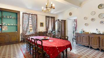 A dining room with a red tablecloth, wooden chairs, a chandelier, and a patterned rug.