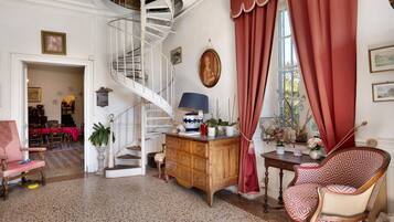 A room with a spiral staircase, a wooden cabinet, a patterned chair, and a dining area with a red tablecloth.