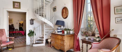 A room with a spiral staircase, a wooden cabinet, a patterned chair, and a dining area with a red tablecloth.
