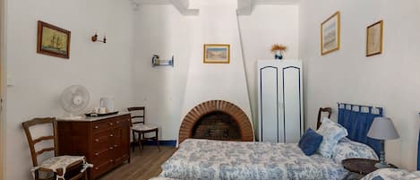 A bedroom with a bed, dresser, chair, and a fireplace.
