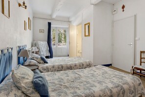 A bedroom with two beds, a chair, a desk, and a bathroom visible through an open door. - Bed and Breakfast 'Chambre Rolland' with Shared Pool, Shared Garden and Wi-Fi (Carcassonne)
