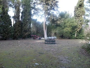 A grassy outdoor area with a circular stone structure, surrounded by tall trees. - Bed and Breakfast 'Chambre Rolland' with Shared Pool, Shared Garden and Wi-Fi (Carcassonne)