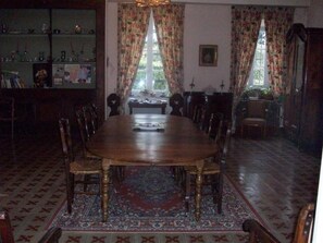 A dining room with a round wooden table surrounded by chairs, a patterned rug, and a bookshelf with various items. - Bed and Breakfast 'Chambre Rolland' with Shared Pool, Shared Garden and Wi-Fi (Carcassonne)
