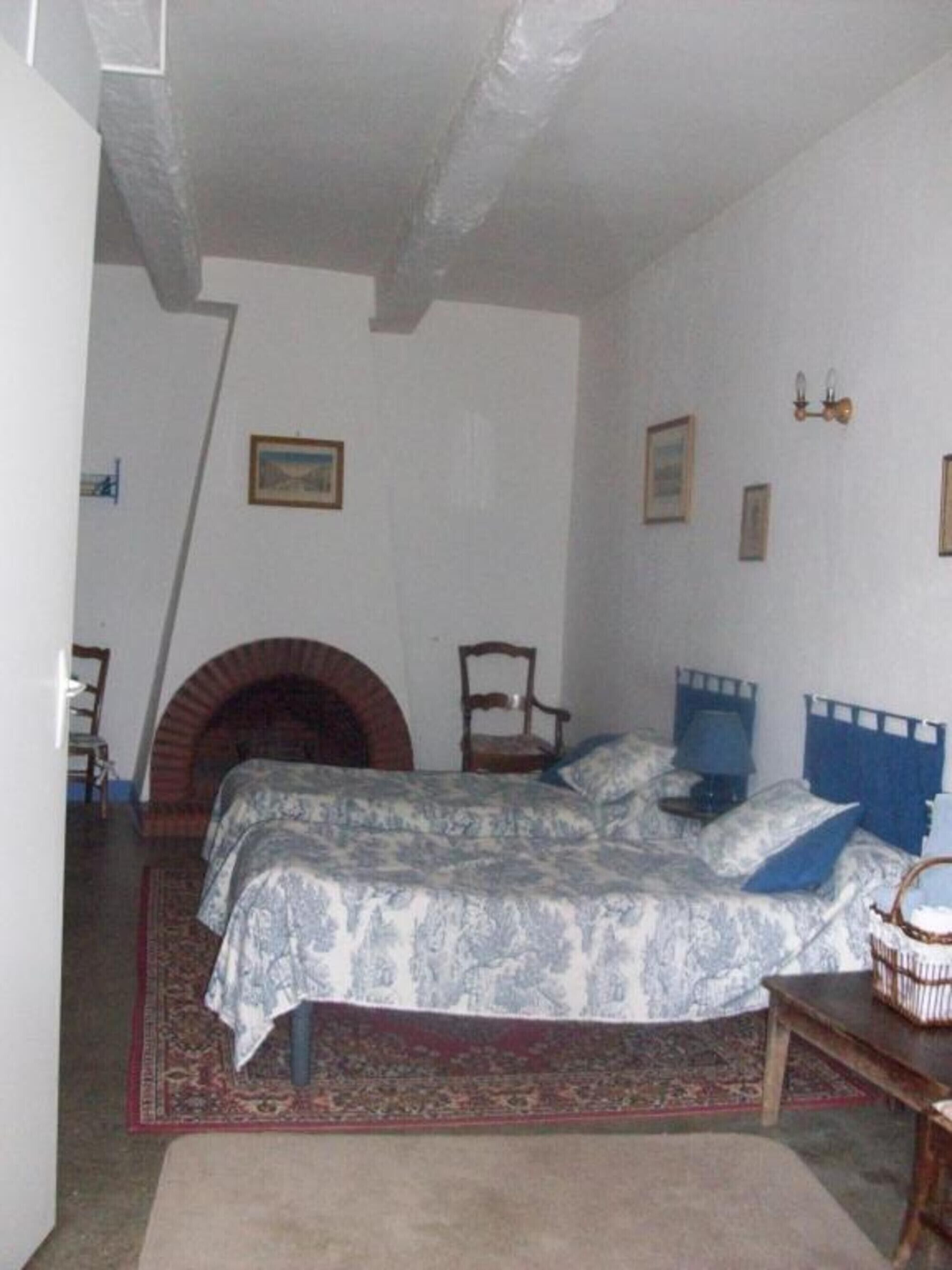 Een slaapkamer met een bed, een open haard, een stoel en een klein tafeltje.