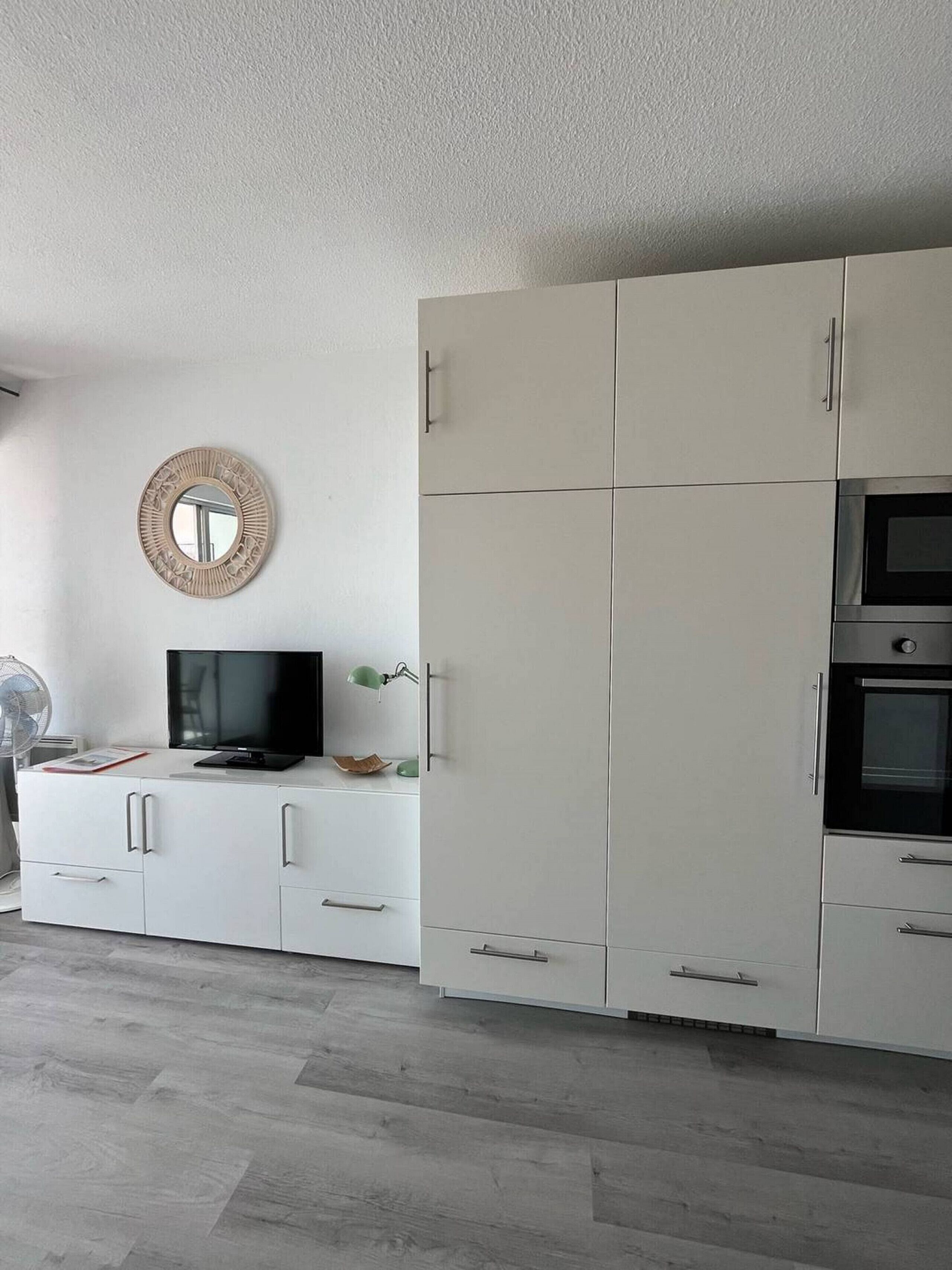 Une cuisine moderne avec des meubles blancs, un four encastré et un téléviseur posé sur une console blanche.