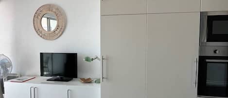 A modern kitchen with white cabinetry, a built-in oven, and a television on a white console.