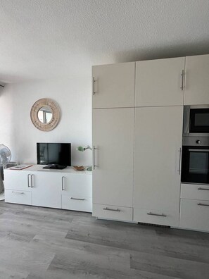 A modern kitchen with white cabinetry, a built-in oven, and a television on a white console.
