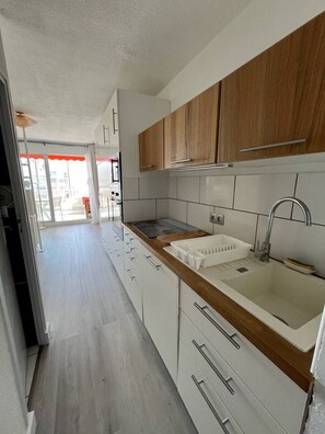 A modern kitchen with white cabinets, a wooden countertop, and a stainless steel sink.