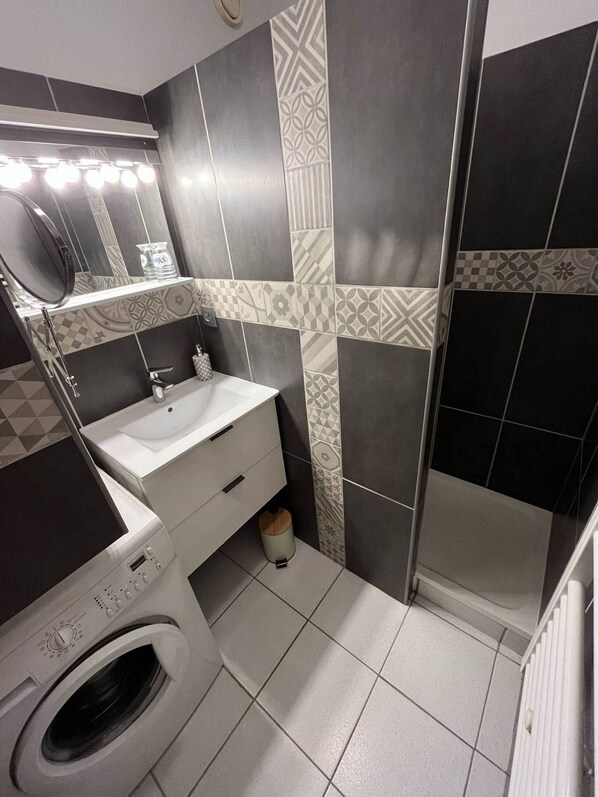 A compact bathroom with a washing machine, a sink, and a mirror.