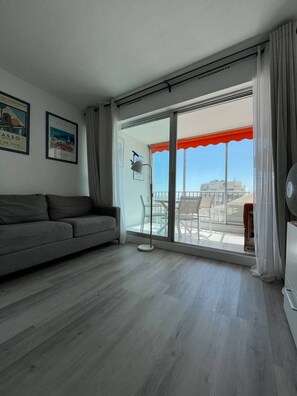 A modern living room with a grey sofa, a glass table, and a balcony with an orange awning.
