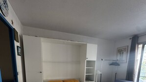 Quarto com cama, guarda-roupa, mesa de cabeceira, abajur e janela.