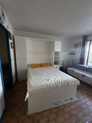 Ett sovrum med en säng, en garderob, ett nattduksbord, en lampa och ett fönster.