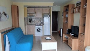 A compact living space with a kitchenette, a blue sofa, a small table, and a TV stand. - Première ligne Plage, studio pour 2 N20 (La Grande-Motte)