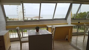 A balcony with a table and chairs, a potted plant, and a view of the sea and a Ferris wheel. - Première ligne Plage, studio pour 2 N20 (La Grande-Motte)