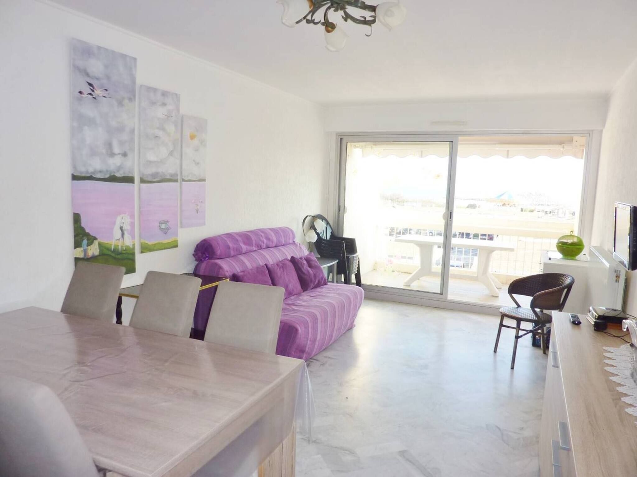 A modern living room with a sofa, dining table, and chairs. There is a balcony with a view.