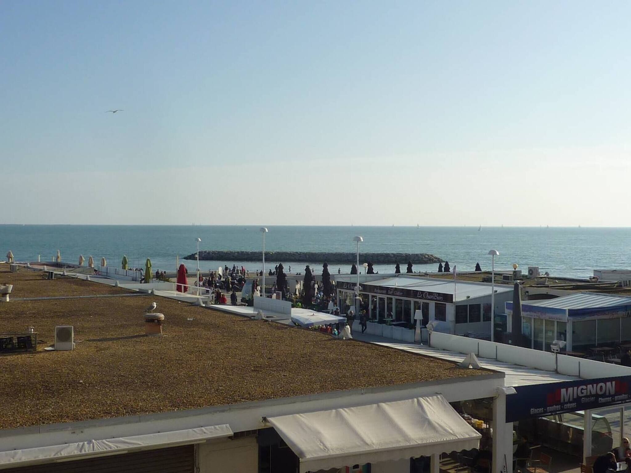A coastal promenade with a pier extending into the sea, a café named 'Le Chariot Bar,' and a Mignon restaurant.