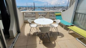 Un balcone con un tavolo rotondo e sedie, una panchina e vista su un porto turistico con barche.