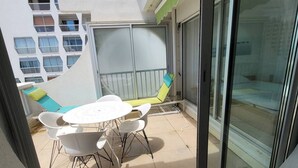 Un balcone con una porta vetrata, un tavolo bianco con sedie e vista su un edificio con numerose finestre.