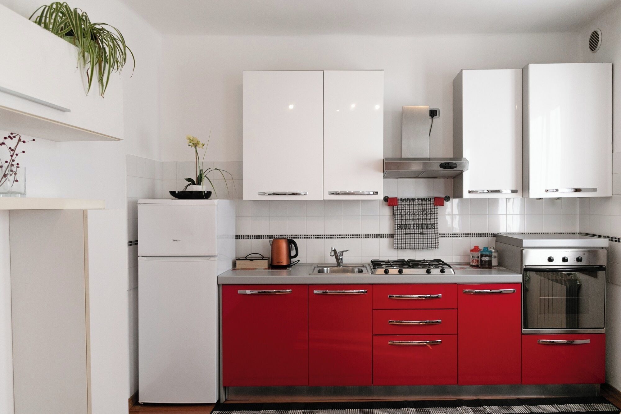 A kitchen with white upper cabinets, red lower cabinets, a stove, an oven, and a sink.