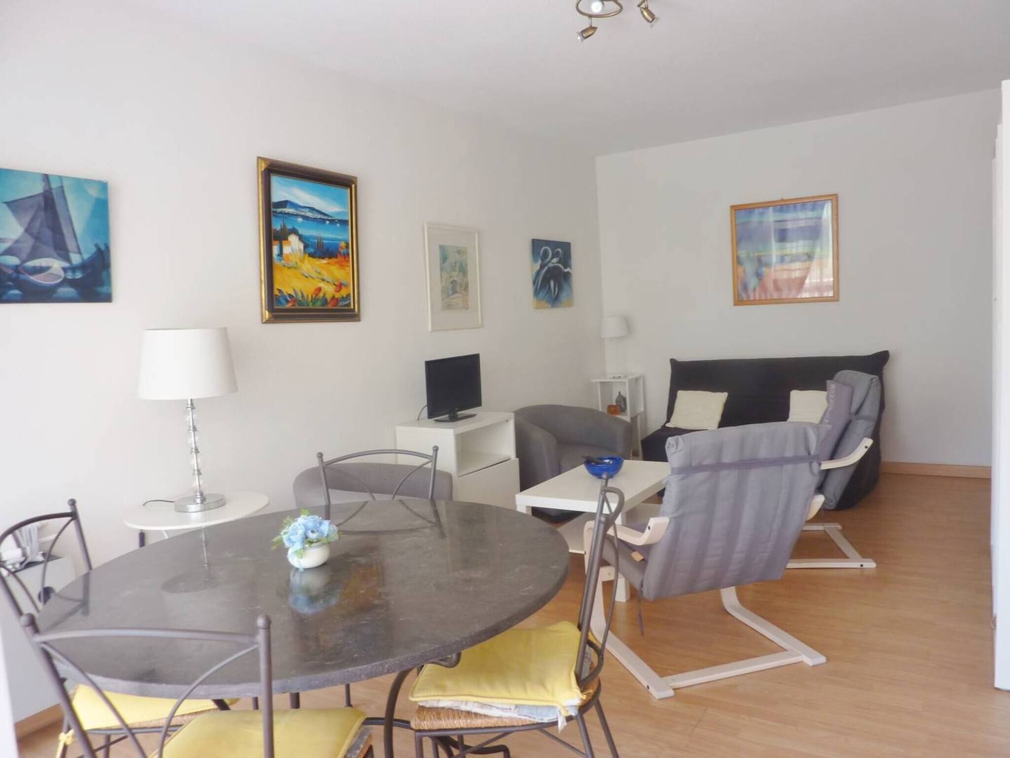Ein modernes Wohnzimmer mit einem runden Esstisch, einer Couch, einem Fernseher und Kunstwerken an den Wänden.