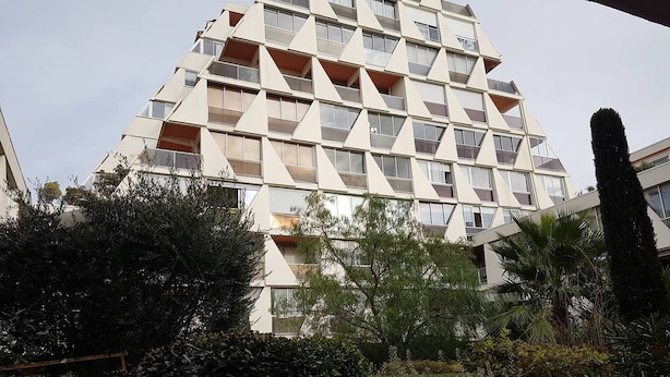 A multi-story building with a geometric facade, balconies, and surrounding greenery. - Coeur de ville, t2 pour 4 N13 (La Grande-Motte)
