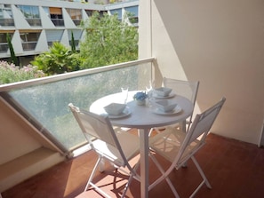 Et lille rundt bord med fire stole på en balkon, med udsigt til en bygning med geometrisk facade og grøntområder.