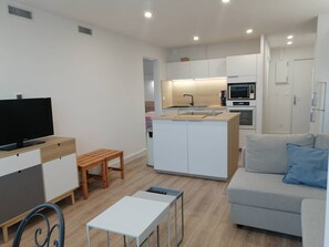 Ein kompakter Wohnbereich mit Küchenzeile, einer Couch, einem Fernseher und einem kleinen Tisch.