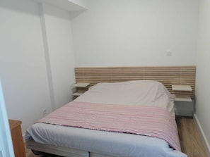 Ein kleiner, schmaler Raum mit einem Einzelbett, einem hölzernen Kopfteil und einem Nachttisch.