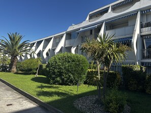 A modern building with balconies, surrounded by well-maintained grass and palm trees. - Appartement pour 4, piscine et parking N75 (La Grande-Motte)
