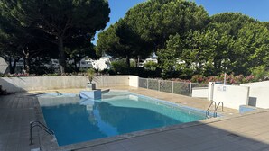 En rektangulär swimmingpool med en kakelbeklädd poolkant, omgiven av en låg, vit mur och träd.
