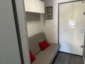 A room with a bed, a door, a light switch, and a power outlet on the wall.