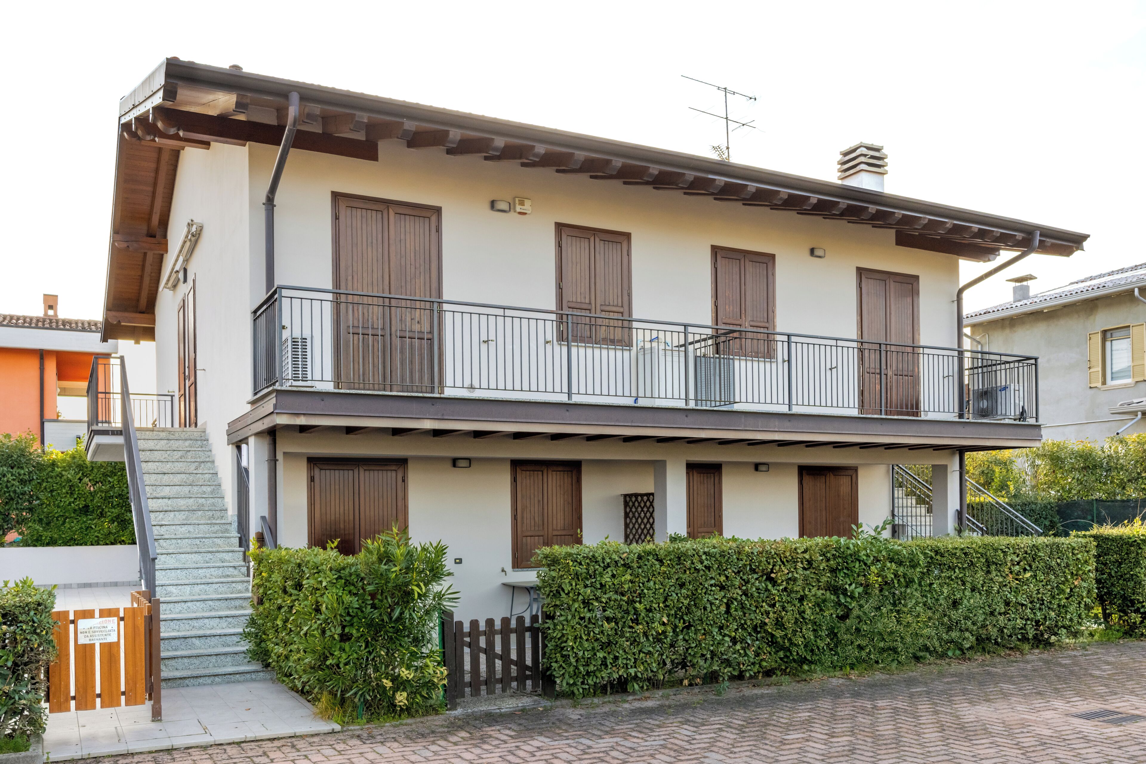 A two-story residential building with a balcony, a staircase, and a hedge in front.