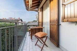 A balcony with a wooden table and chairs, a small stool, and a door with a patterned curtain. - Gardenia P1-10 by Wonderful Italy (Lombardia)