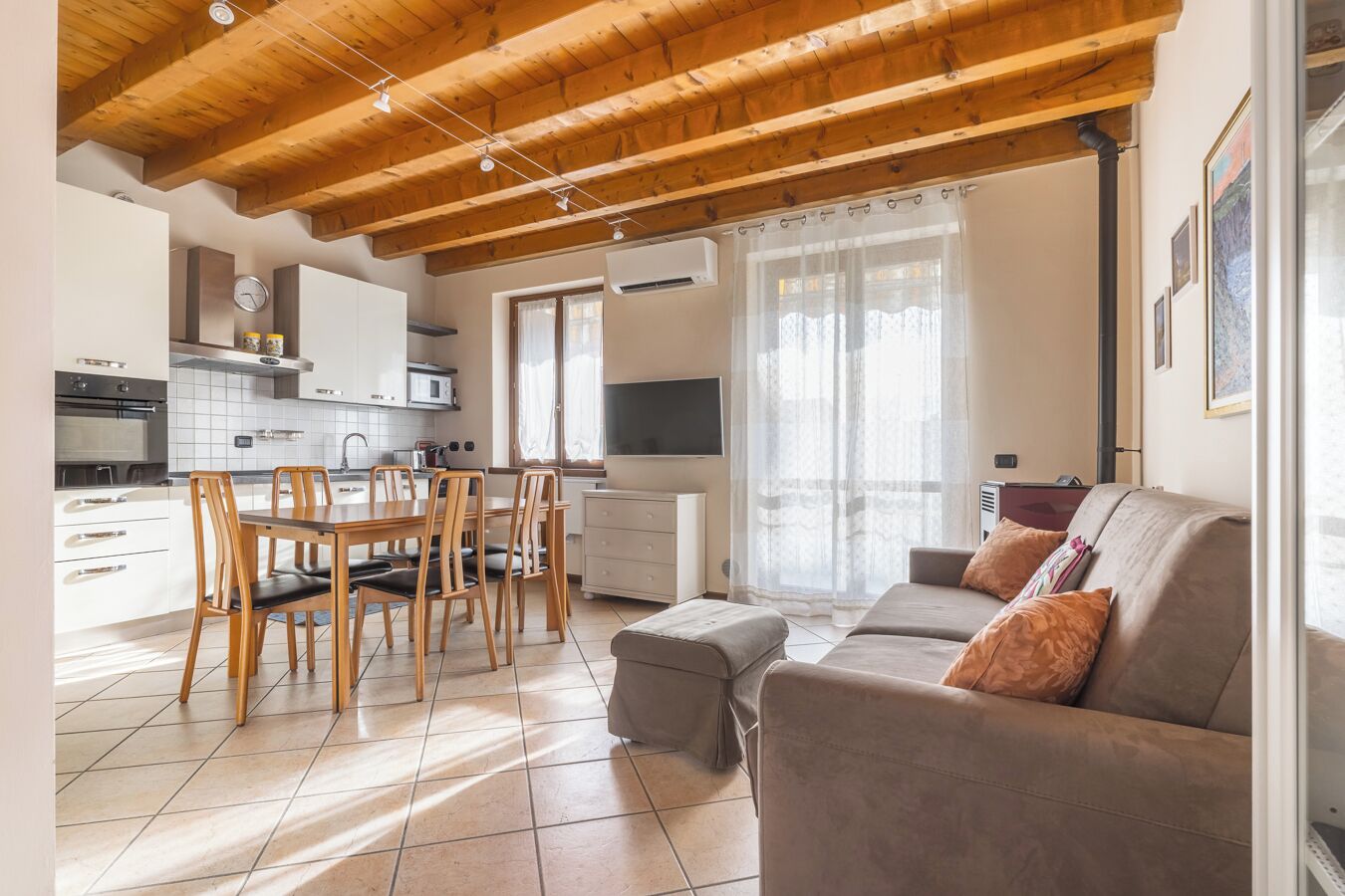 A modern kitchen with white cabinets, a dining table with chairs, a sofa with cushions, and a TV.