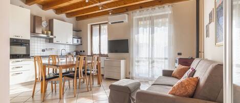 A modern kitchen with white cabinets, a dining table with chairs, a sofa with cushions, and a TV.