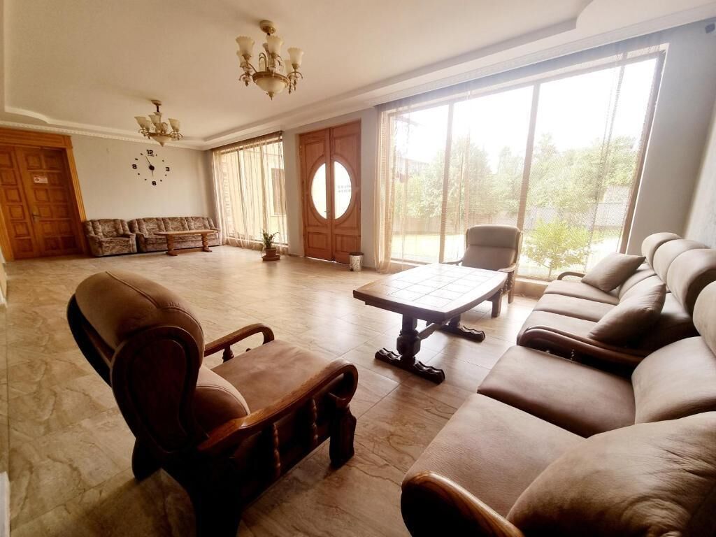 A spacious living room with a large window, a sofa set, a coffee table, and a chandelier.