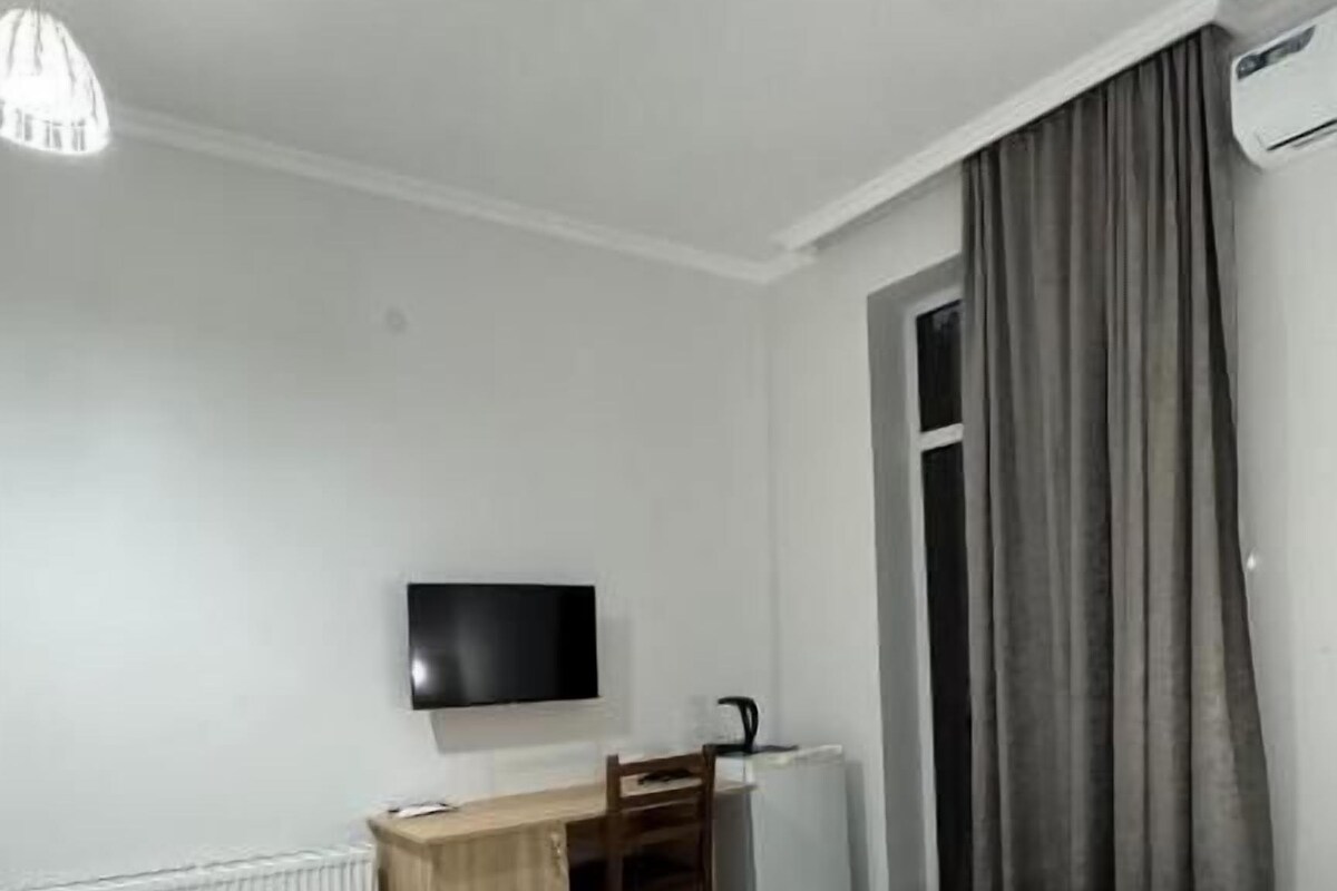 A hotel room with two beds, a desk, a chair, a television, and a window with curtains.