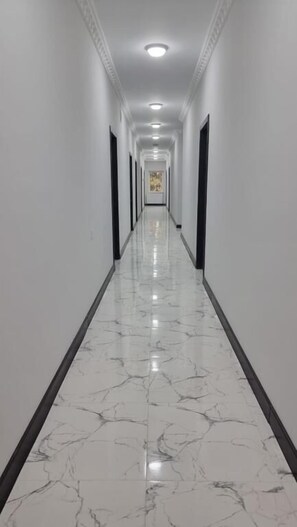 A long, narrow hallway with white walls and a marble floor.