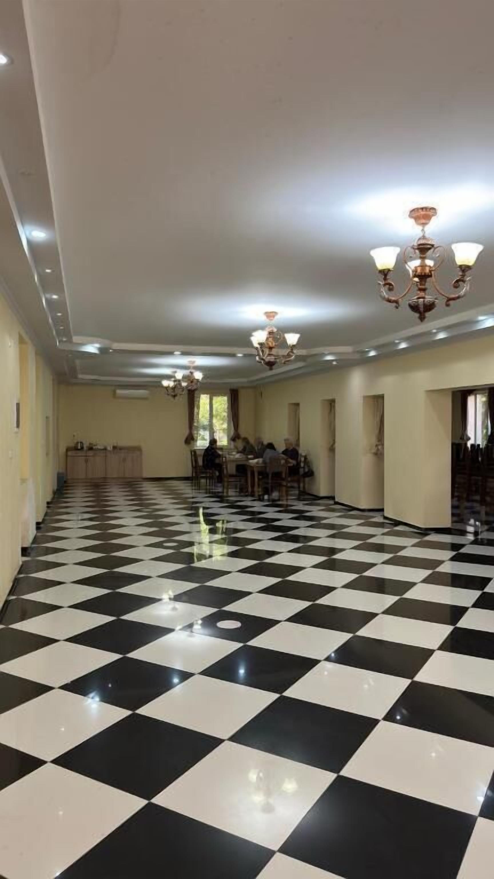 Un hall d’hôtel avec un sol à carreaux, des lustres et un groupe de personnes assises autour d’une table.