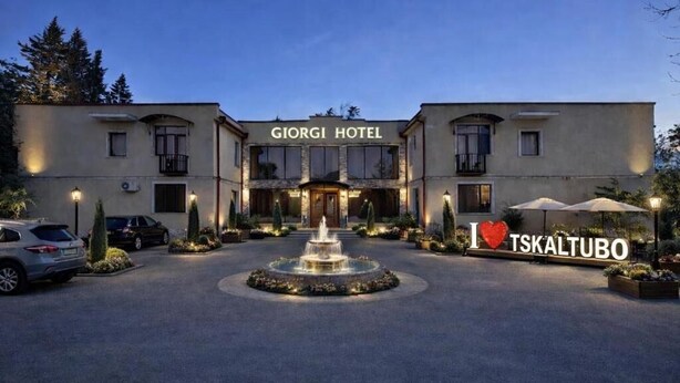 A hotel named 'Giorgi Hotel' with a fountain in the center, surrounded by parked cars and potted plants.