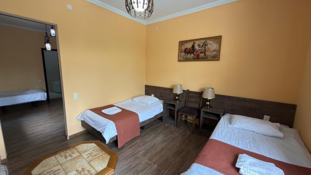 Una habitación de hotel con dos camas individuales, un cabecero de madera, una mesita pequeña, dos lámparas de noche y un cuadro en la pared.