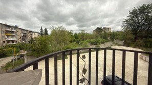 A balcony with a metal railing, overlooking a courtyard with greenery and buildings in the background.