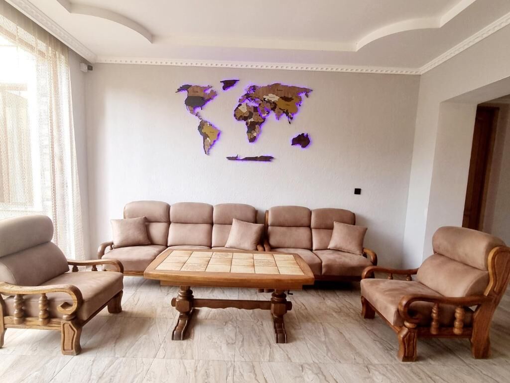 A living room with a beige sofa set, wooden coffee table, and two armchairs. A world map is displayed on the wall.
