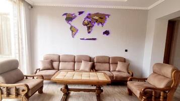 A living room with a beige sofa set, wooden coffee table, and two armchairs. A world map is displayed on the wall.