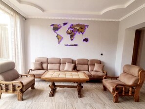 A living room with a beige sofa set, wooden coffee table, and two armchairs. A world map is displayed on the wall.