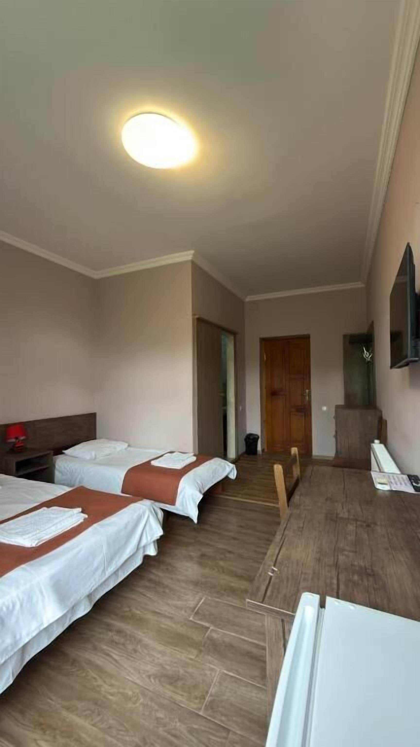Habitación de hotel con dos camas, un escritorio, una silla, un televisor y una puerta que da a otra habitación.