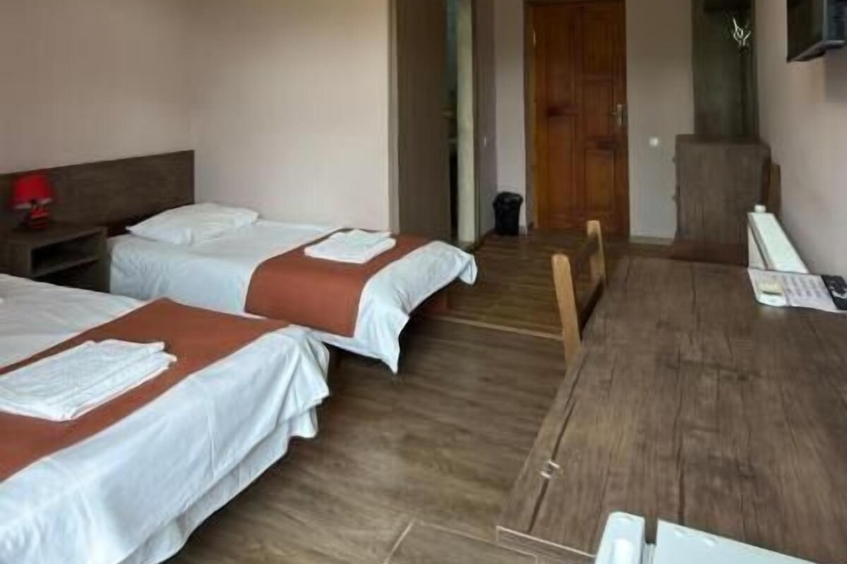 A hotel room with two beds, a desk, a chair, a television, and a door leading to another room.