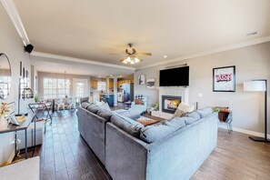 A spacious living room with a large sectional sofa, a fireplace, and a television mounted on the wall. - The Brick Beauty | Dog-Friendly & Fenced Yard (Bentonville)
